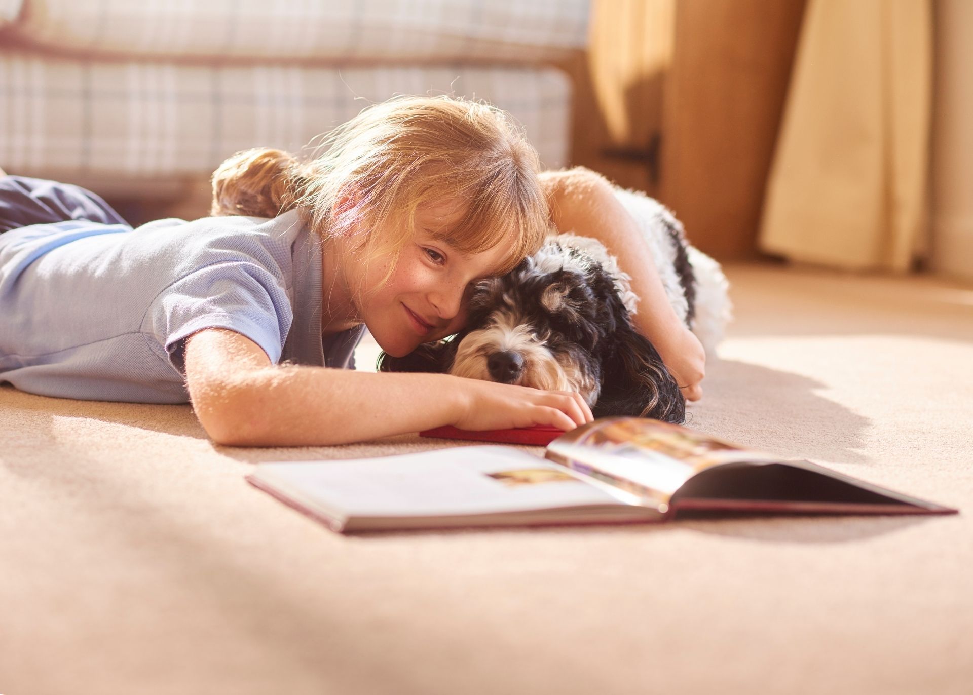 Smiling young girl and her black and white small dog laying on floor and reading a book