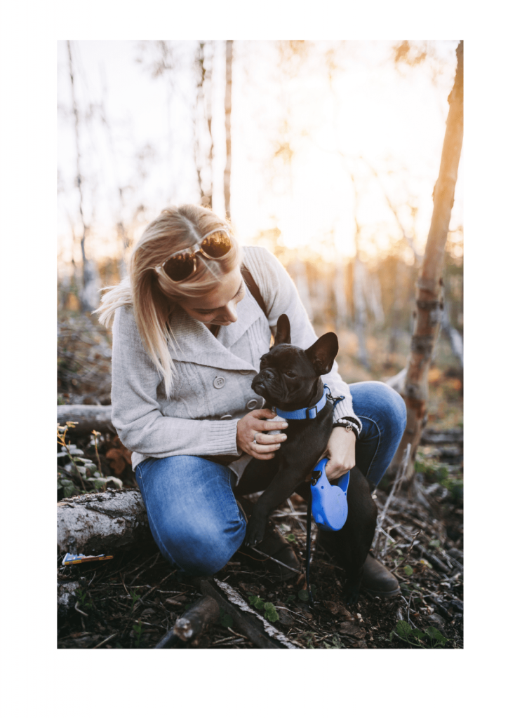 Woman in jeans and boots in woods with black french bulldog