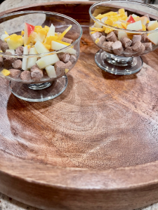 Two small raised glass bowls with hydrated freeze dried raw, apple bits, and shredded cheddar cheese. Bowls are sitting on a round wood tray.