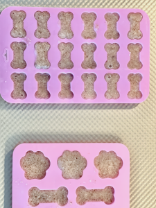 Fresh mushroom broth for dogs in pink silicone dog bone molds on gold cookie tray.