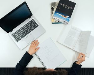 Person at desk with books, notebooks, and laptop