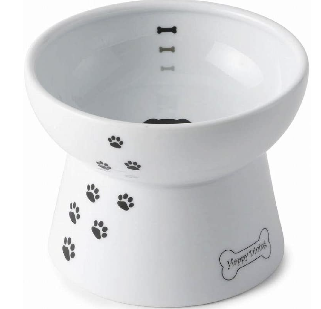 White ceramic dog bowl on raised ceramic stand with black paw prints up the side